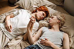 Gay couple holding hands and looking at each other while laying on bed