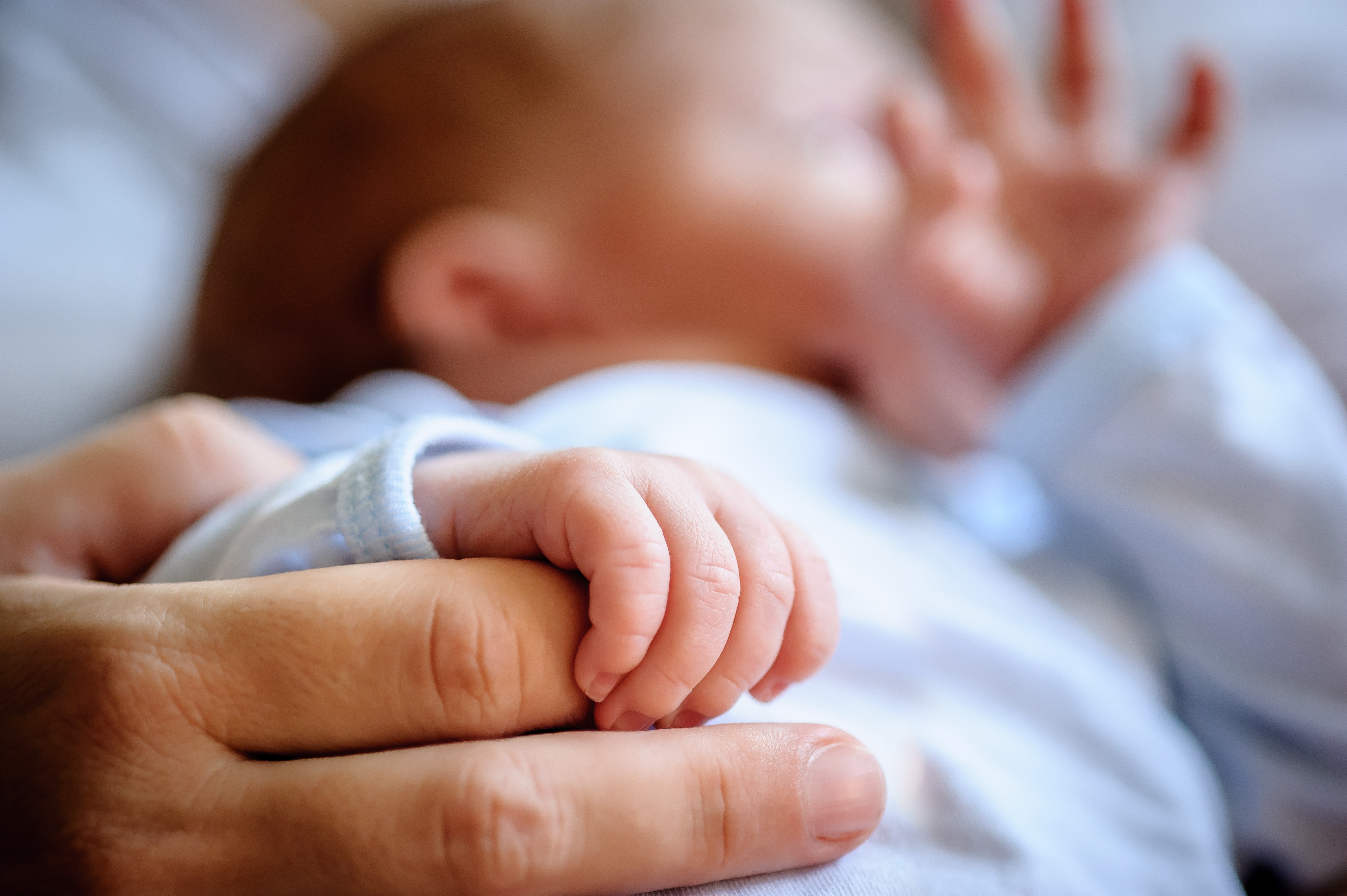 Close-up detail macro view of baby holding on to mom's finger with his little hand. Soft child skin. Love and family emotion Macro of baby holding on mother finger with little hand
